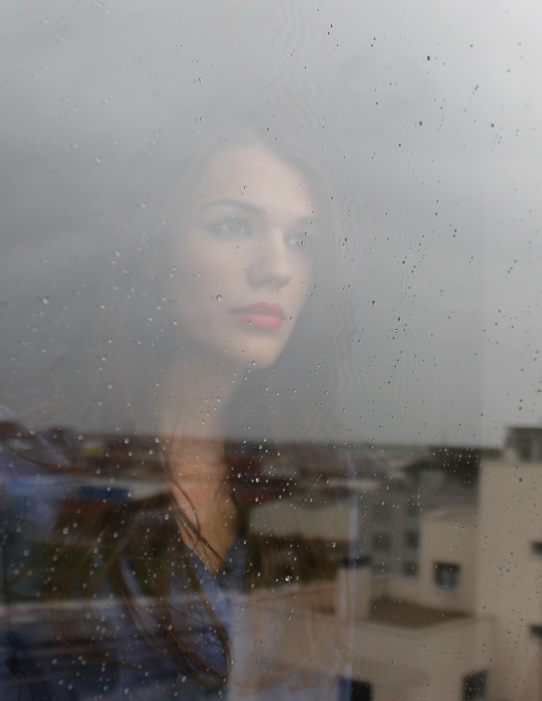 chica triste tras cristal con lluvia